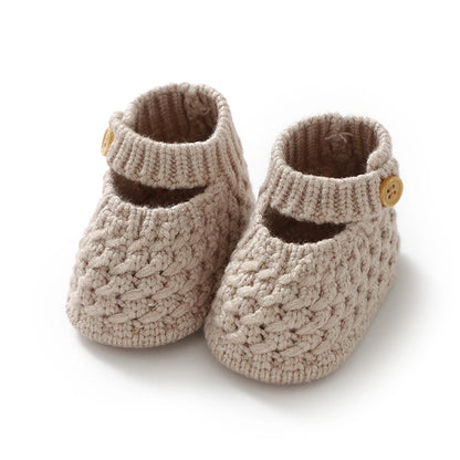 Pair of soft beige knit Mary Jane baby booties on a white background.