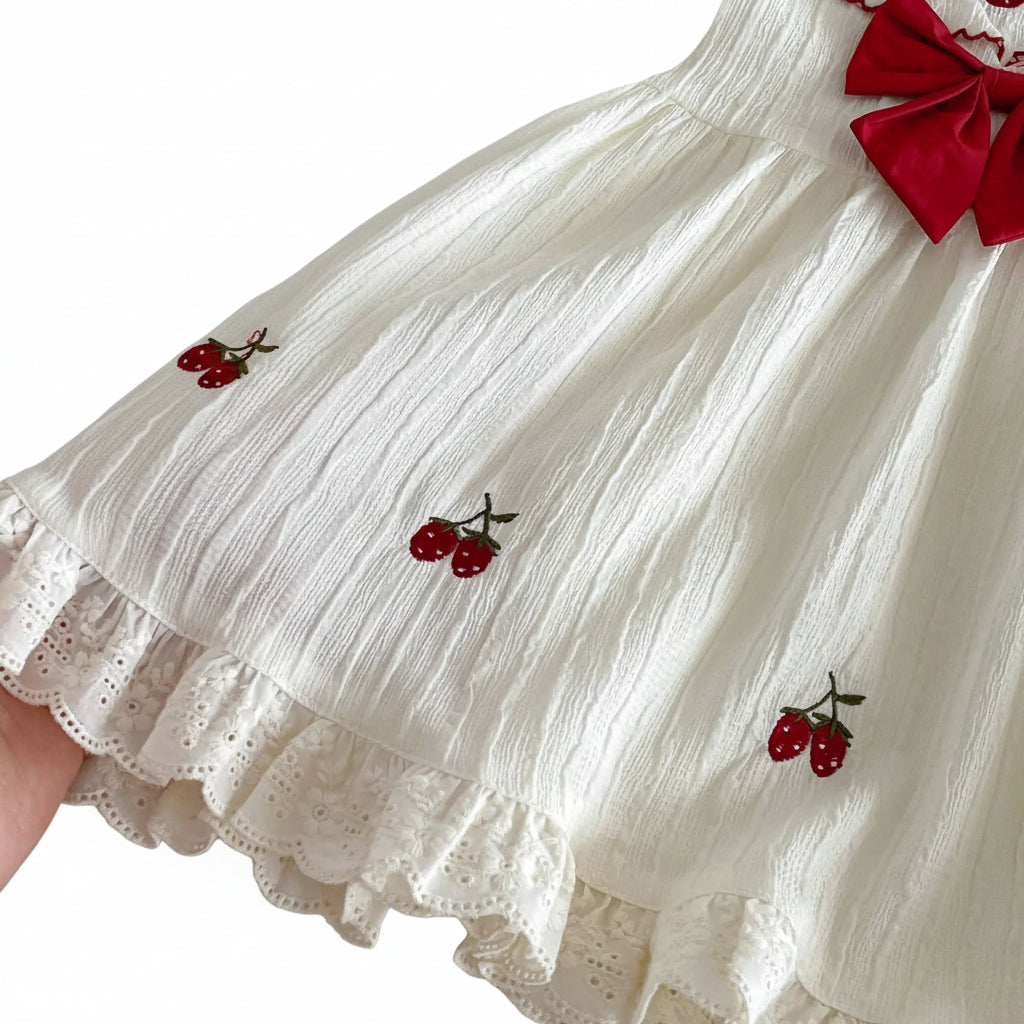 Detail shot of the lower skirt of the Kidsely dress showing the delicate strawberry embroidery layout on the cream textured fabric.