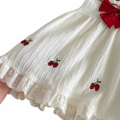 Detail shot of the lower skirt of the Kidsely dress showing the delicate strawberry embroidery layout on the cream textured fabric.