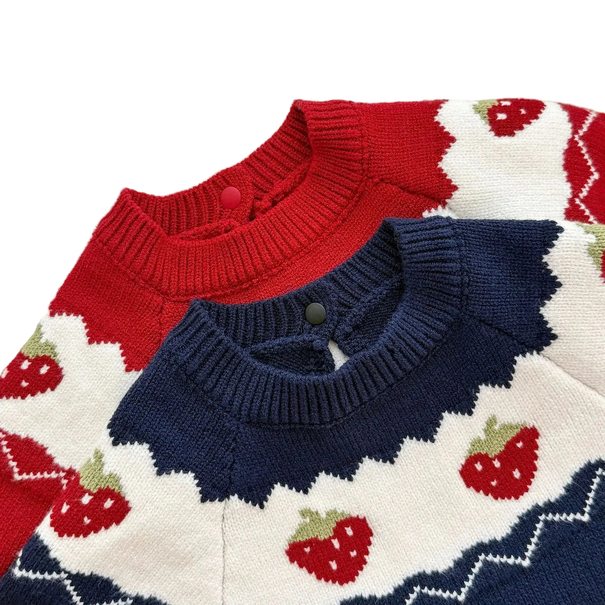 Close-up of the ribbed crew neck, back button closure, and white color-blocked yoke with knit strawberries on the red and navy baby rompers.