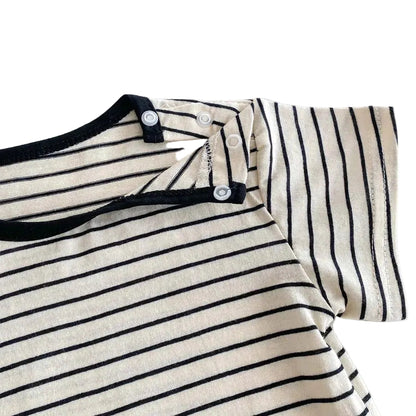 Close up showing the convenient shoulder snap buttons on the black and white striped baby t-shirt for easy dressing.