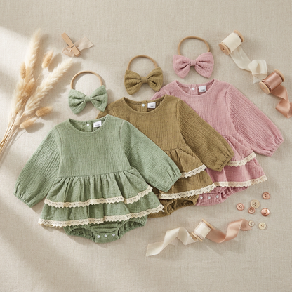 Styled aesthetic flat lay featuring sage green, mustard, and pink infant girl lace rompers and headbands surrounded by dried floral props and ribbon.