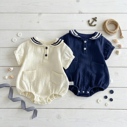 Aesthetic flat lay of Sea Salt and Deep Sea rompers styled with a toy anchor, rope, and buttons on a white wood background.