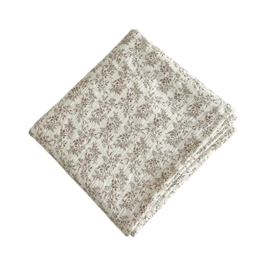Folded taupe botanical leaf cotton muslin swaddle blanket on a clean white background.