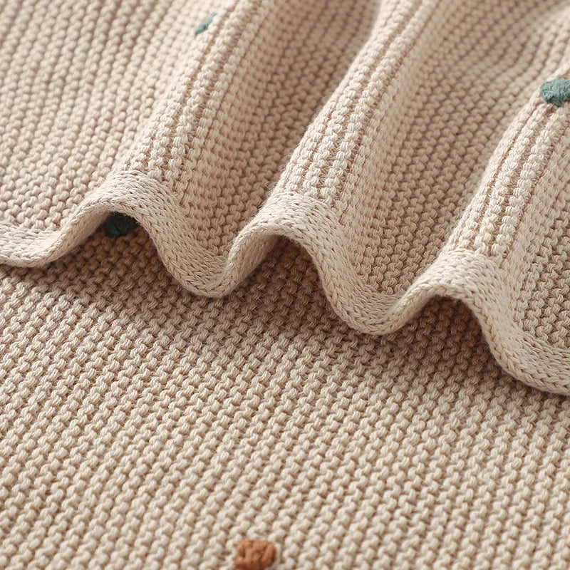 Extreme close-up of the breathable garter stitch weave and a wavy fold of the Toasted Almond cotton baby blanket, highlighting a small textured colored dot.