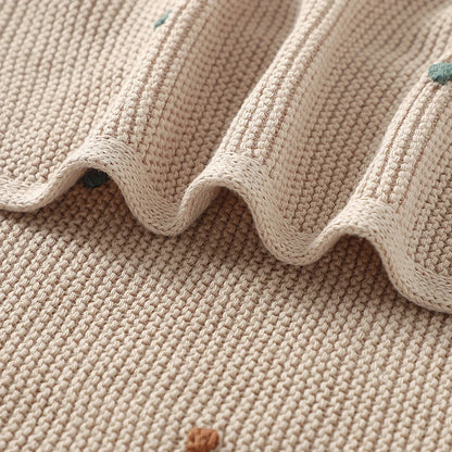 Extreme close-up of the breathable garter stitch weave and a wavy fold of the Toasted Almond cotton baby blanket, highlighting a small textured colored dot.
