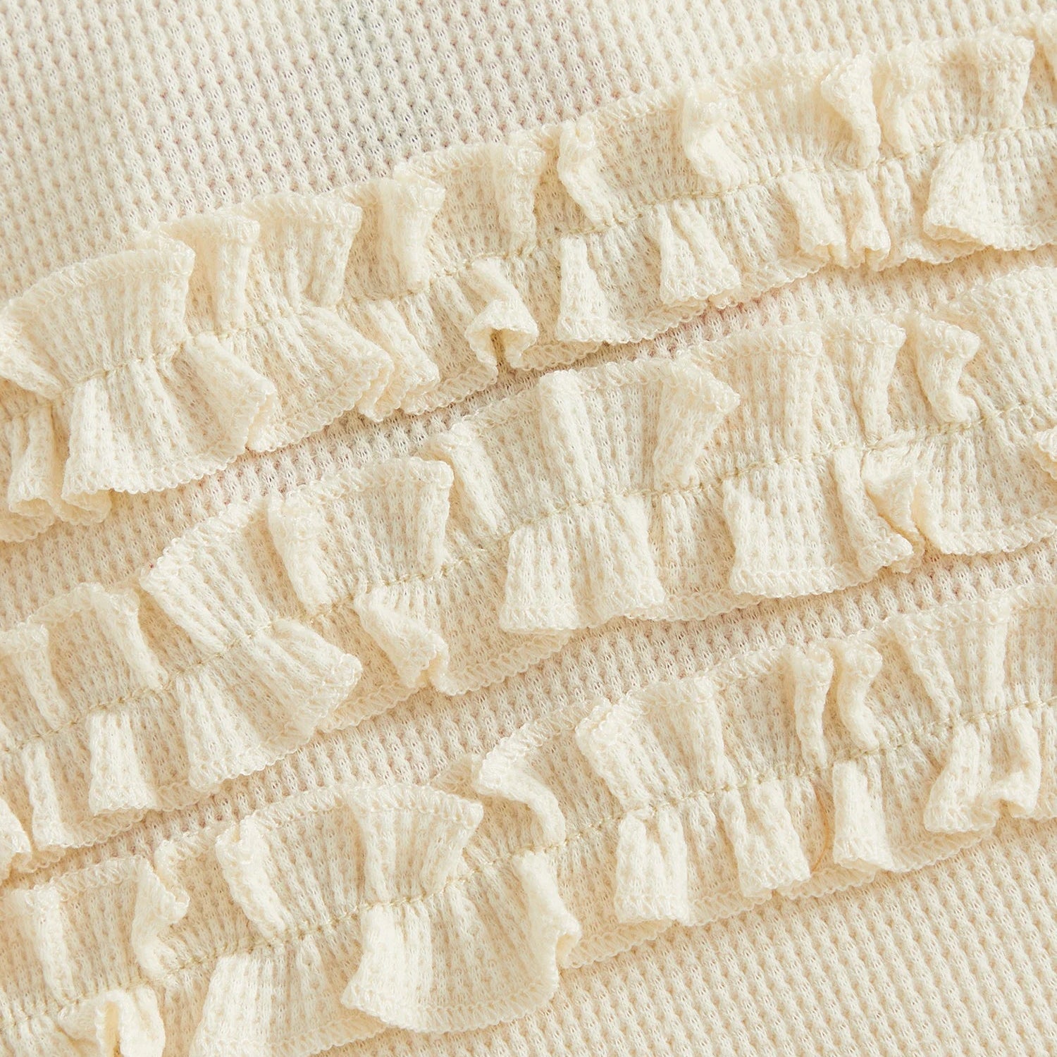 Close-up of the three-tiered ruffle design on the back of the cream ribbed cotton baby romper.