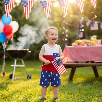 Happy toddler boy wearing a red, white, and blue 4th of July outfit while playing outside at a summer BBQ with patriotic decorations.