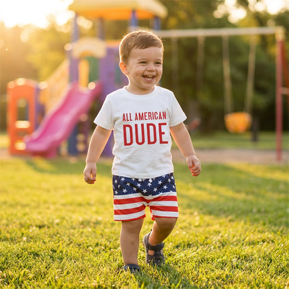 Happy toddler boy walking outdoors wearing the white "All American Dude" 4th of July t-shirt and patriotic shorts set.