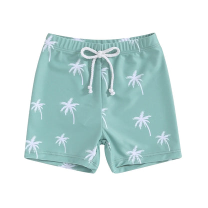 Toddler boys teal green swimming shorts with an all-over white minimalist palm tree print and a white adjustable drawstring waist.
