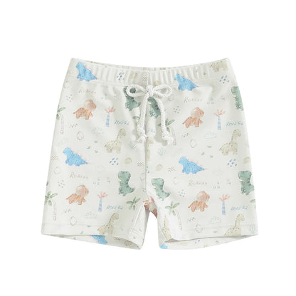 Baby and toddler boys white swim trunks featuring soft watercolor-style pastel dinosaurs, palm trees, and "Roar" text graphics with a white drawstring.