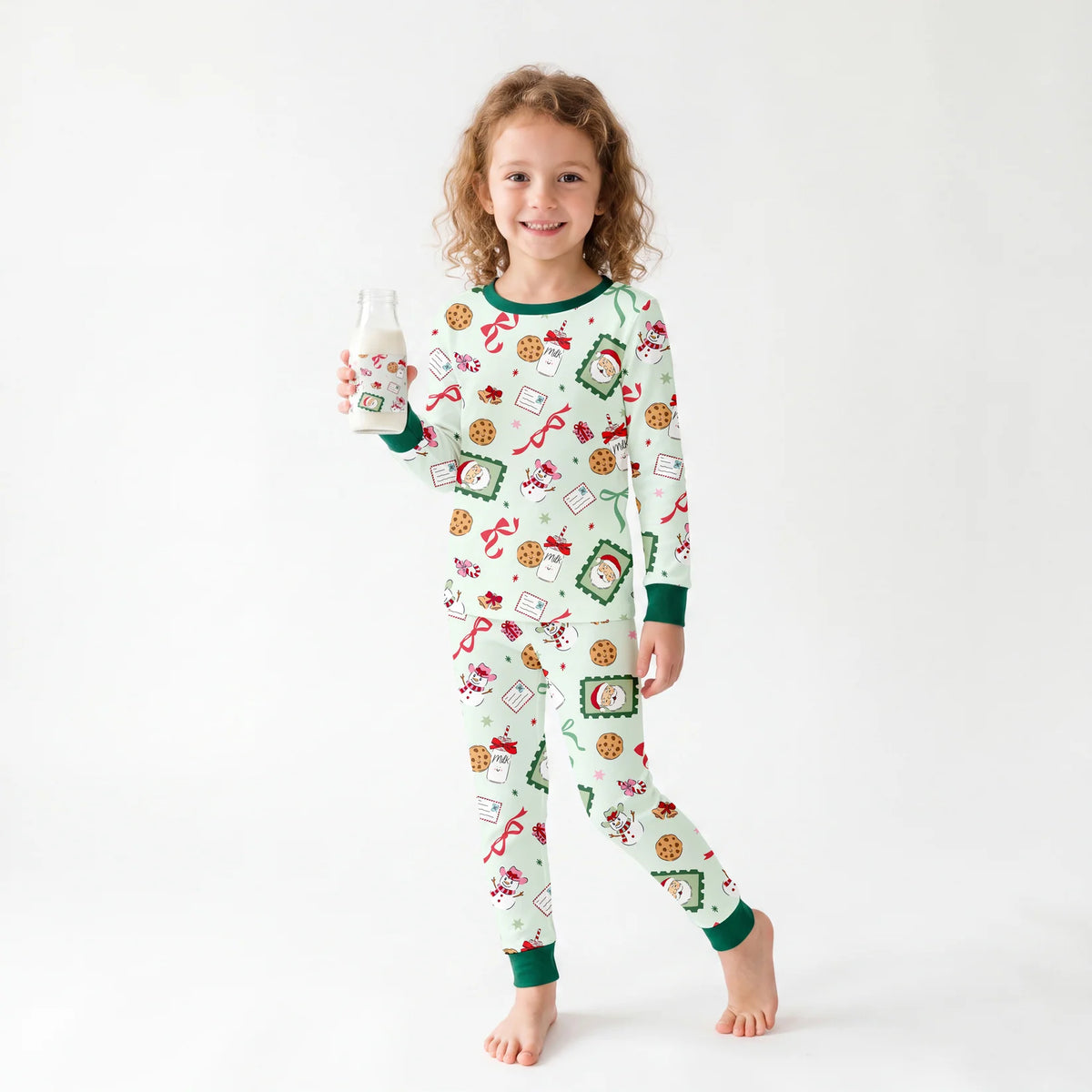 Toddler wearing two-piece Sweet Treats Christmas bamboo pajama set holding a milk bottle in a studio setting