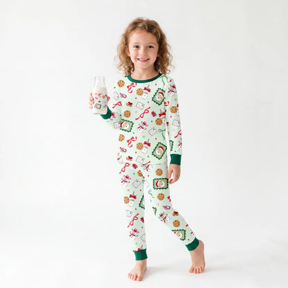 Toddler wearing two-piece Sweet Treats Christmas bamboo pajama set holding a milk bottle in a studio setting