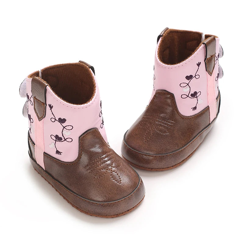 Top-down view of standing pink and brown faux leather baby booties with detailed western stitching on the toe.