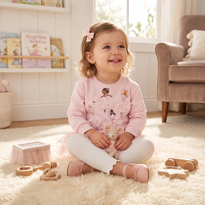 Smiling toddler girl wearing pink ballerina 3D tulle sweatshirt and white leggings set sitting on a rug with toys.