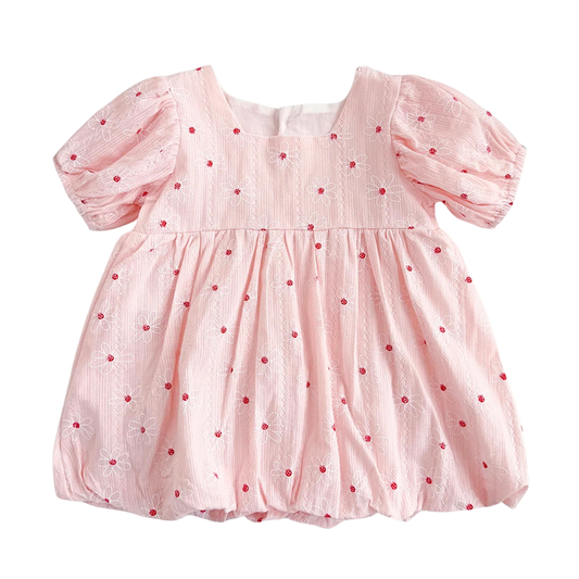 Vintage white baby girl bubble dress featuring red floral embroidery, puff sleeves, and a gathered hem on a neutral textured background.
