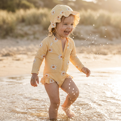 Toddler girl wearing a rash guard swimsuit with a daisy print at the beach