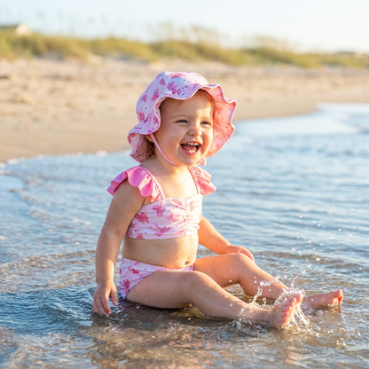 A toddler girl wearing a pink bow ruffle bikini while playing in the water at the beach