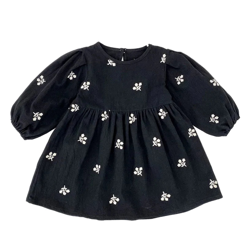 Front view of a toddler girls black smock dress featuring white floral embroidery and long puff sleeves.