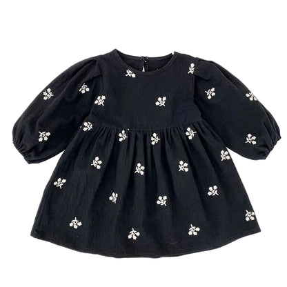 Front view of a toddler girls black smock dress featuring white floral embroidery and long puff sleeves.