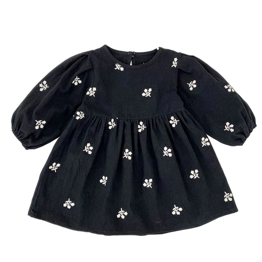 Front view of a toddler girls black smock dress featuring white floral embroidery and long puff sleeves.