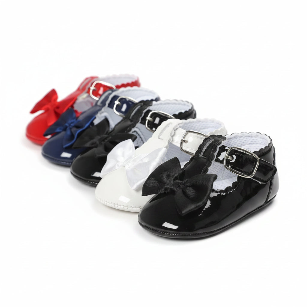 A collection of toddler girl T-strap dress shoes in red, navy blue, white, and black patent leather lined up diagonally.