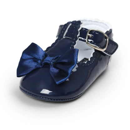 Profile view of a single toddler navy blue patent leather T-strap dress shoe showcasing the side buckle and satin bow details.