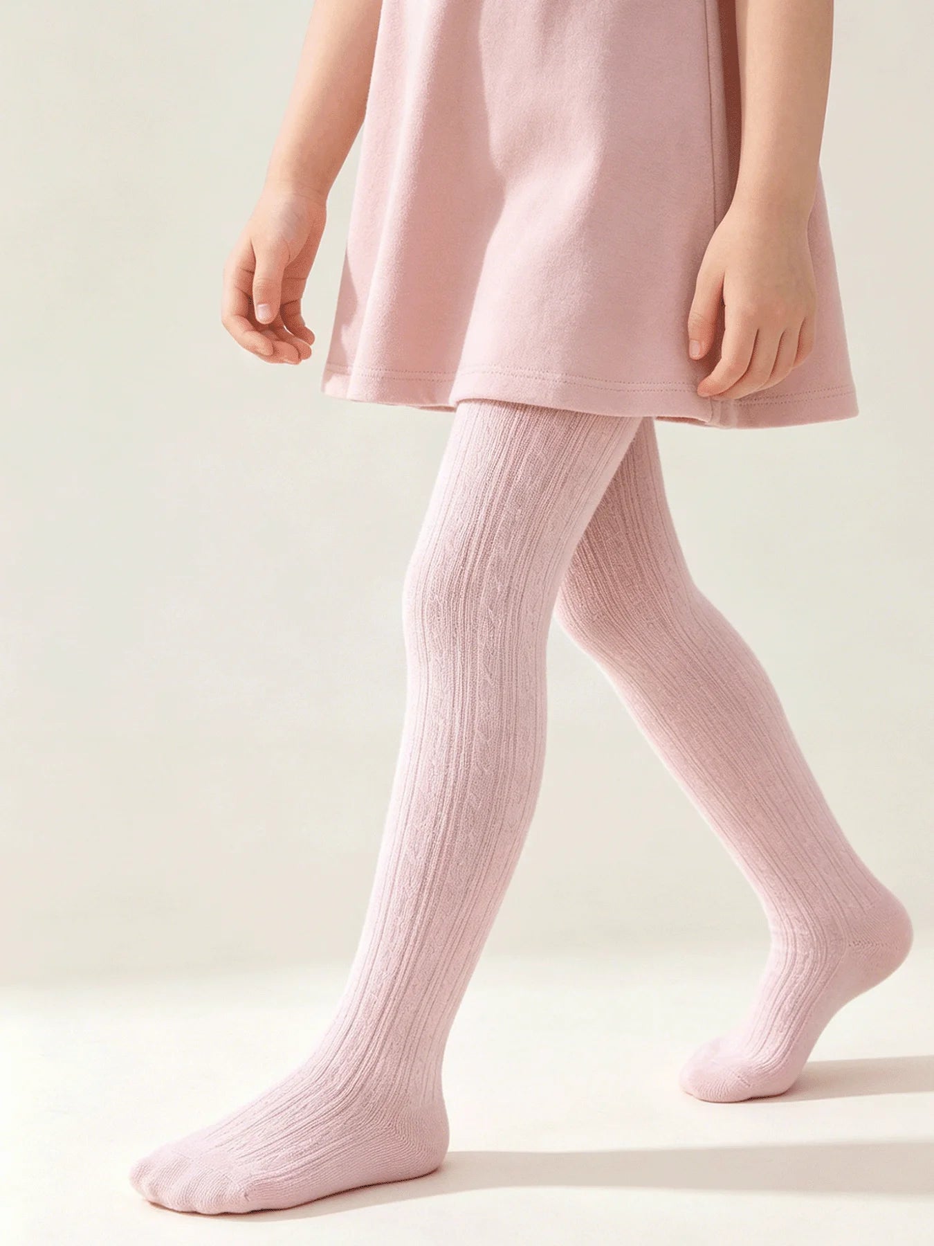 Close up of a little girl's legs walking in soft pink cable knit tights, showing the braided texture.