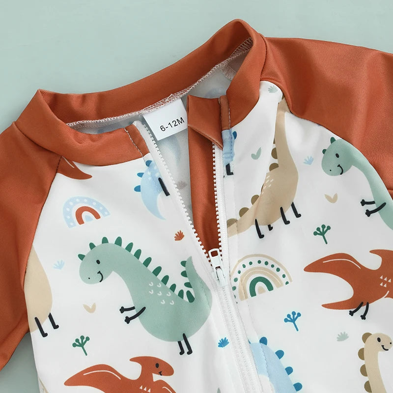 Close-up of the easy-pull front half-zipper and neck guard on the baby dinosaur swimsuit, highlighting the terracotta fabric and earth-tone dino pattern.