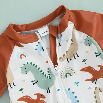 Close-up of the easy-pull front half-zipper and neck guard on the baby dinosaur swimsuit, highlighting the terracotta fabric and earth-tone dino pattern.