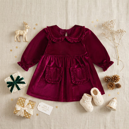 Wine red long sleeve velvet toddler dress flat lay styled with holiday ornaments and baby shoes.