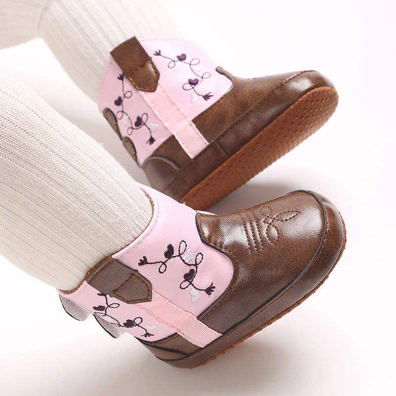 Close up of a toddler's feet in white knit tights wearing pink and brown faux leather western booties.