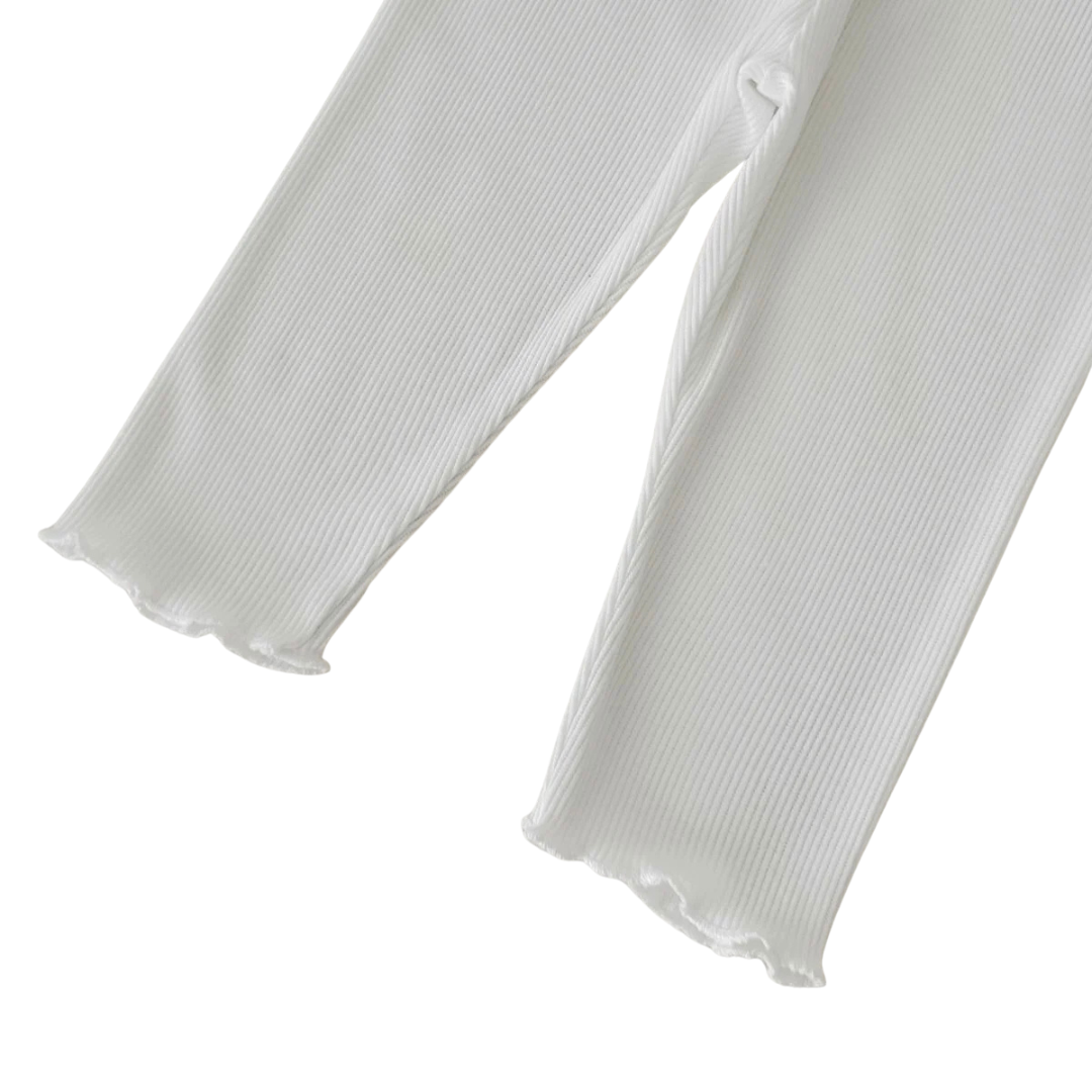 Close-up of soft white ribbed leggings with lettuce-trim leg cuffs for baby girls.