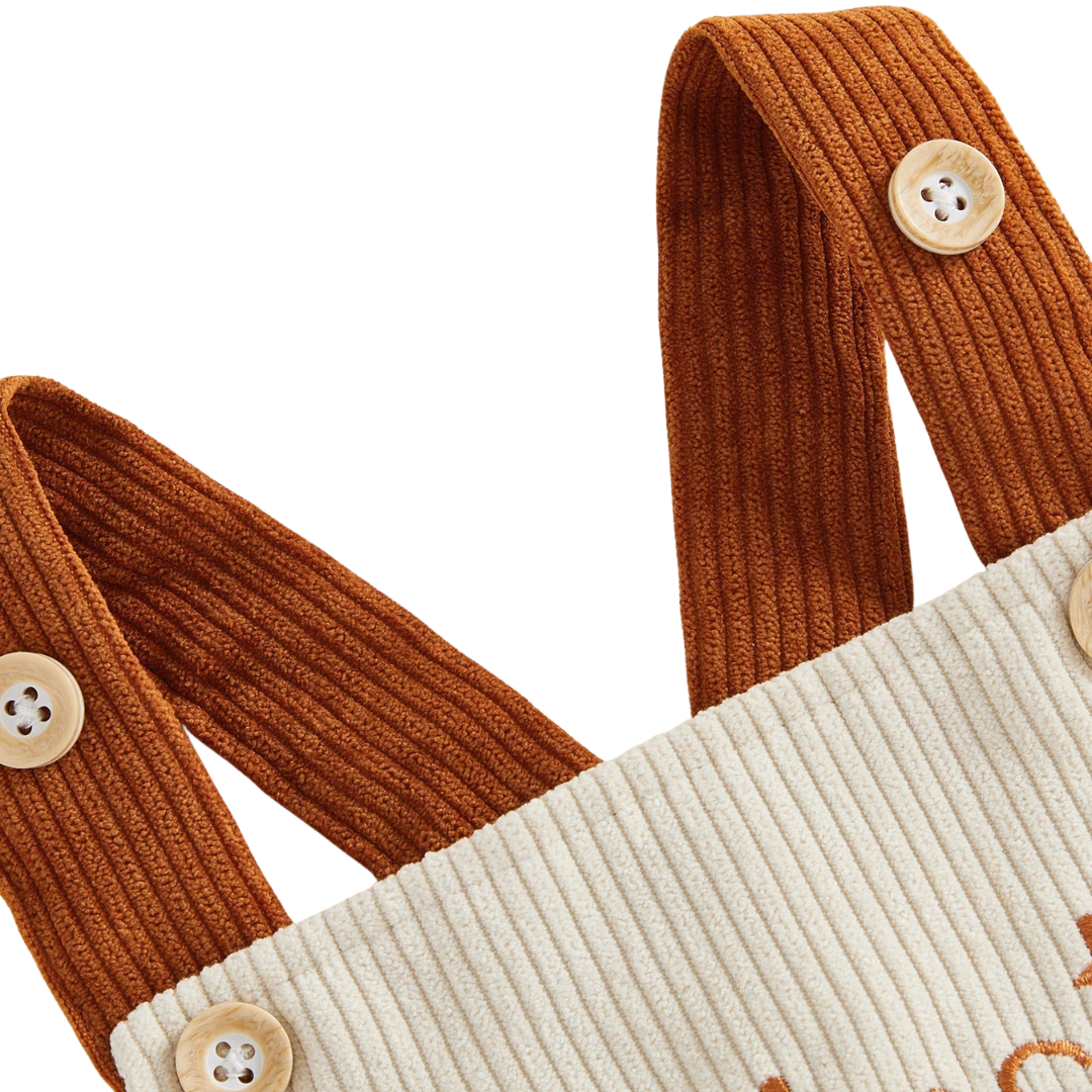 Close-up of the contrasting brown corduroy shoulder straps and button details on the beige baby Thanksgiving jumpsuit.