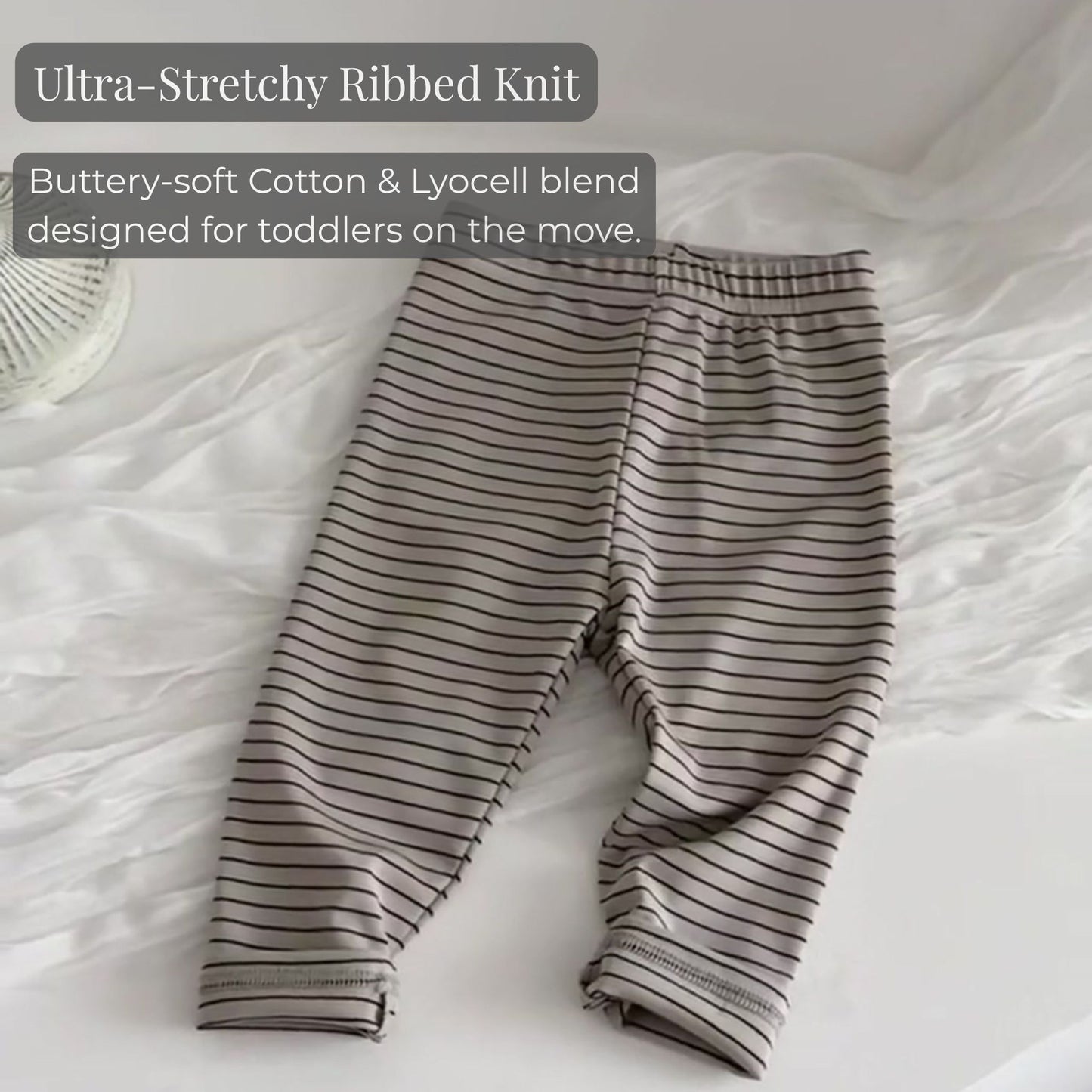 A close-up showing the ultra-stretchy ribbed knit fabric of the baby's horizontal striped leggings resting on a bed.