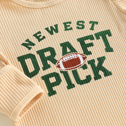 Close-up detail of the green "Newest Draft Pick" text and football graphic on a beige ribbed baby romper.