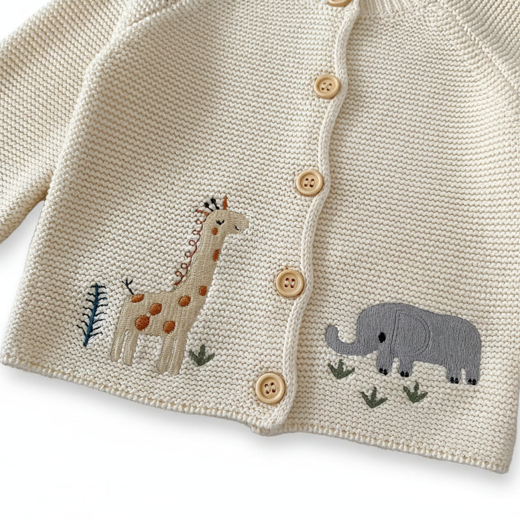 Detailed view of the safari-themed giraffe and grey elephant embroidery stitched on the bottom hem of the cream knit infant sweater.