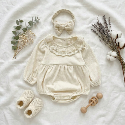 Elegant fall boutique flat lay of the cream baby girl bubble romper set, matching bow headband, baby shoes, and decorative dried florals.