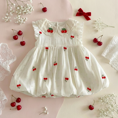 Boutique flat lay of a cherry embroidered baby girl dress styled with red cherries and velvet bows.