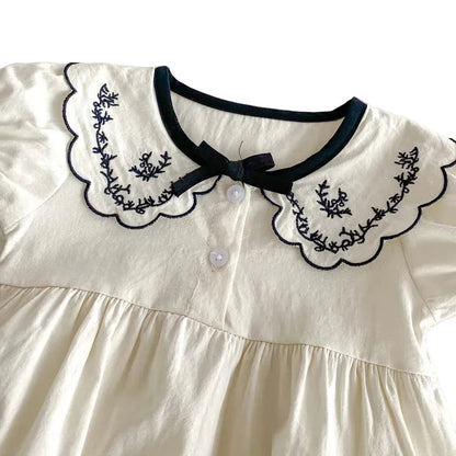 Close-up detail of the black floral embroidery on the ivory scalloped lapel collar and delicate center bow.