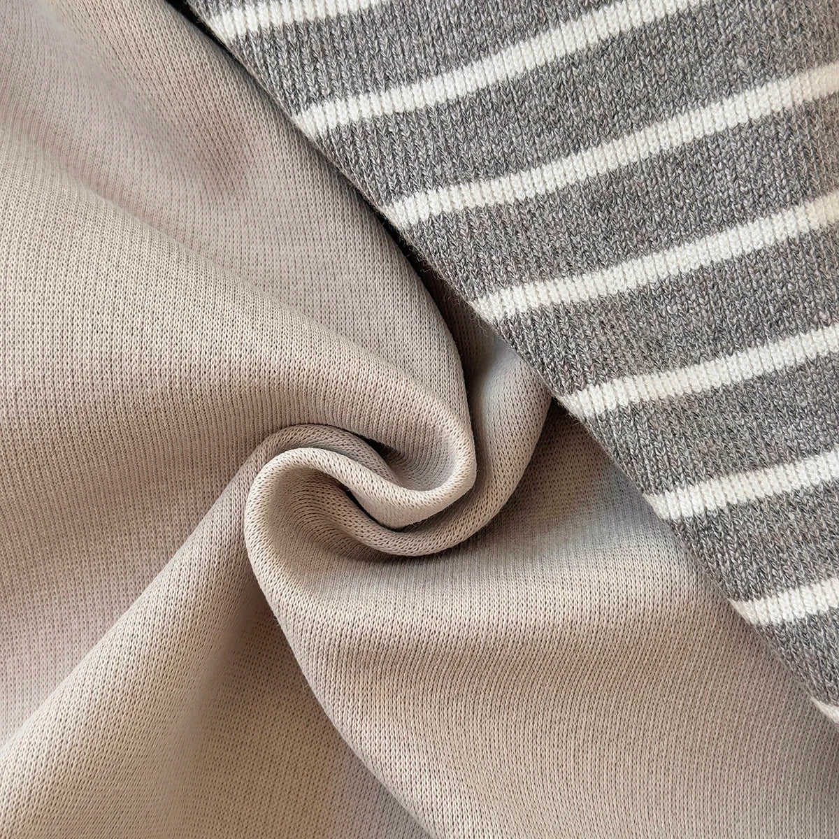 Close-up showing the soft, folded fabric texture of both the solid beige material and the grey and white striped material.