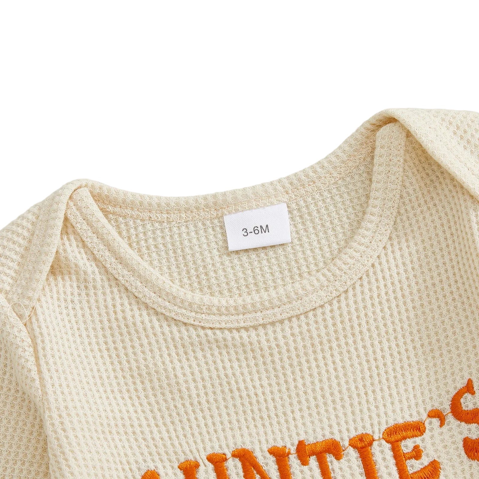Close-up of the round neckline and shoulder of the beige baby romper, highlighting the soft waffle knit texture and inner sizing tag.