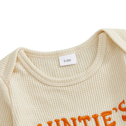 Close-up of the round neckline and shoulder of the beige baby romper, highlighting the soft waffle knit texture and inner sizing tag.