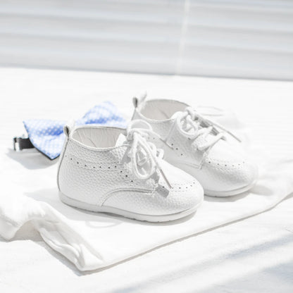 Flat lay of Kidsely white pebbled infant dress shoes styled next to a light blue formal baby bowtie.