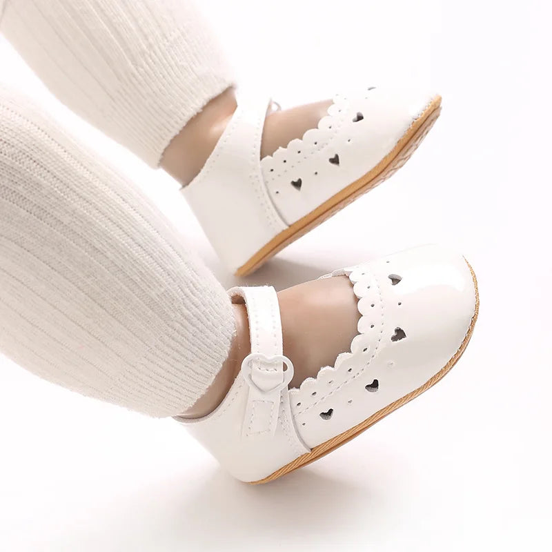 Baby feet wearing white scalloped Mary Jane flats for special occasions.