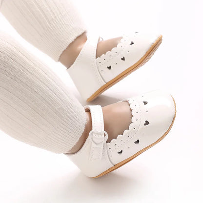 Baby feet wearing white scalloped Mary Jane flats for special occasions.
