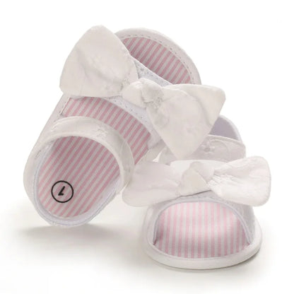 Front view of white baby girl eyelet bow sandals showing the adjustable ankle strap and striped footbed.