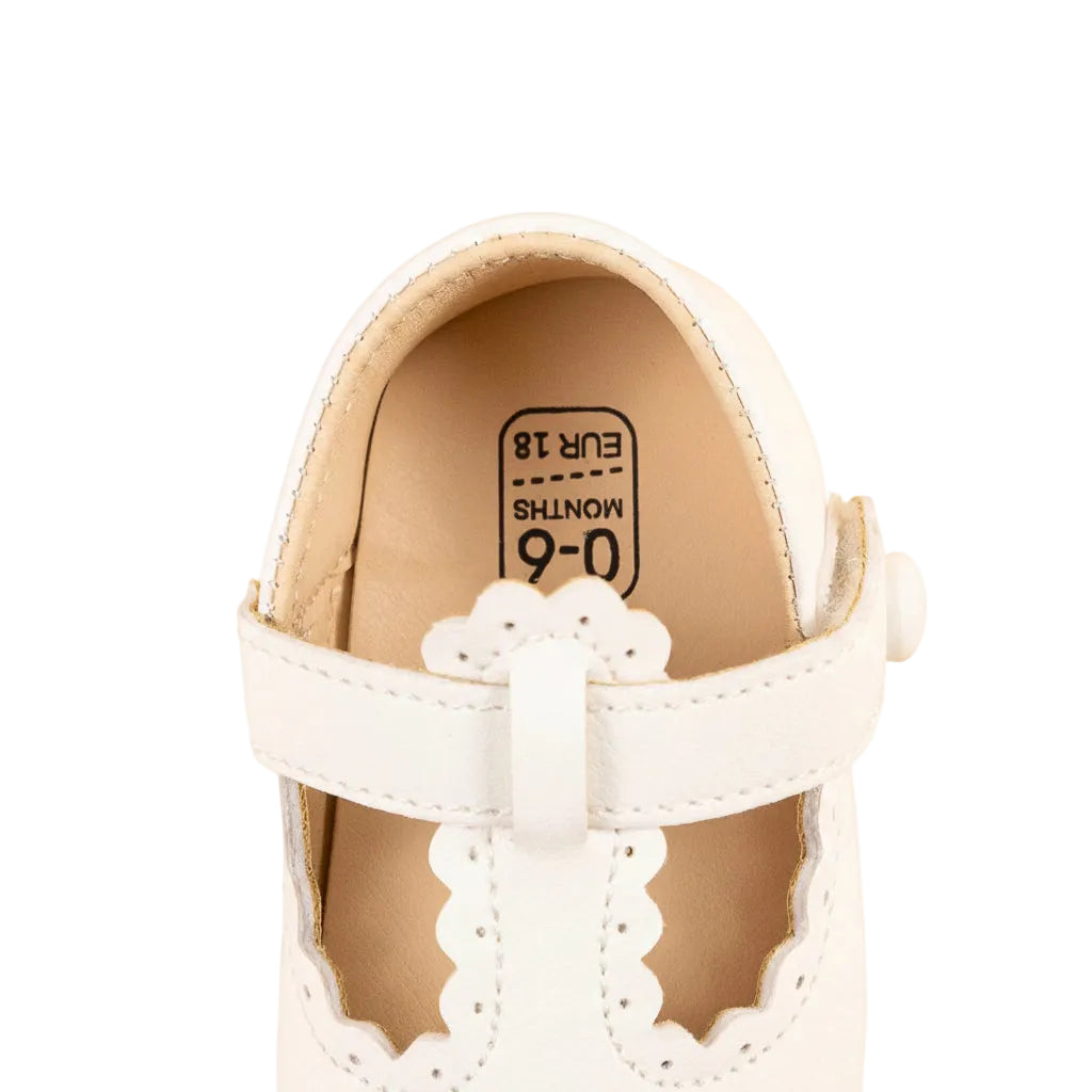 Top-down close-up view of the heel and T-strap of a white infant crib shoe.