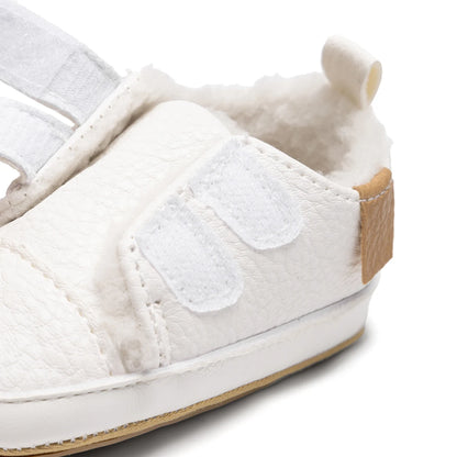 Close-up of the white infant sneaker with opened hook-and-loop straps demonstrating the easy slip-on, wide-opening design.