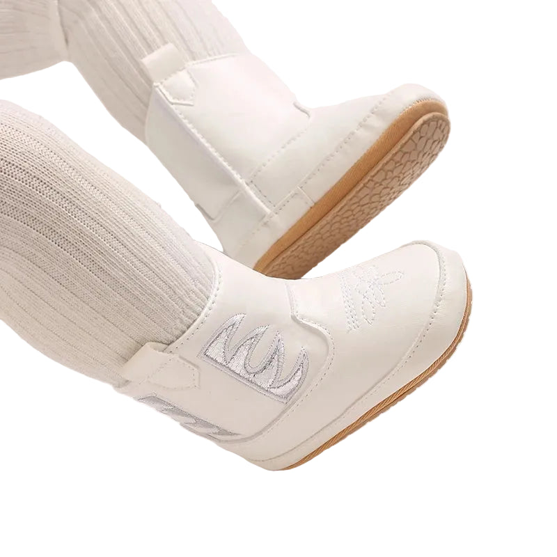 Close up of white baby cowgirl boots on an infant's feet, showing the flexible, textured anti-slip rubber soles.
